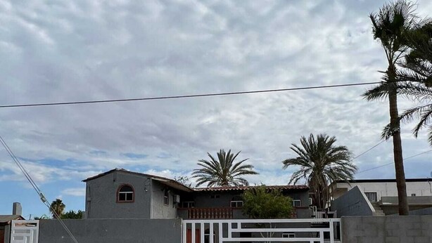 A residential building with a gated entrance, a concrete wall, and a palm tree in the background. - Menta Condo (San Felipe)