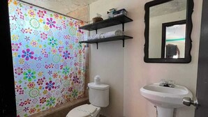 A bathroom with a toilet, a sink, a mirror, and a shower curtain with a floral pattern. - Menta Condo (San Felipe)