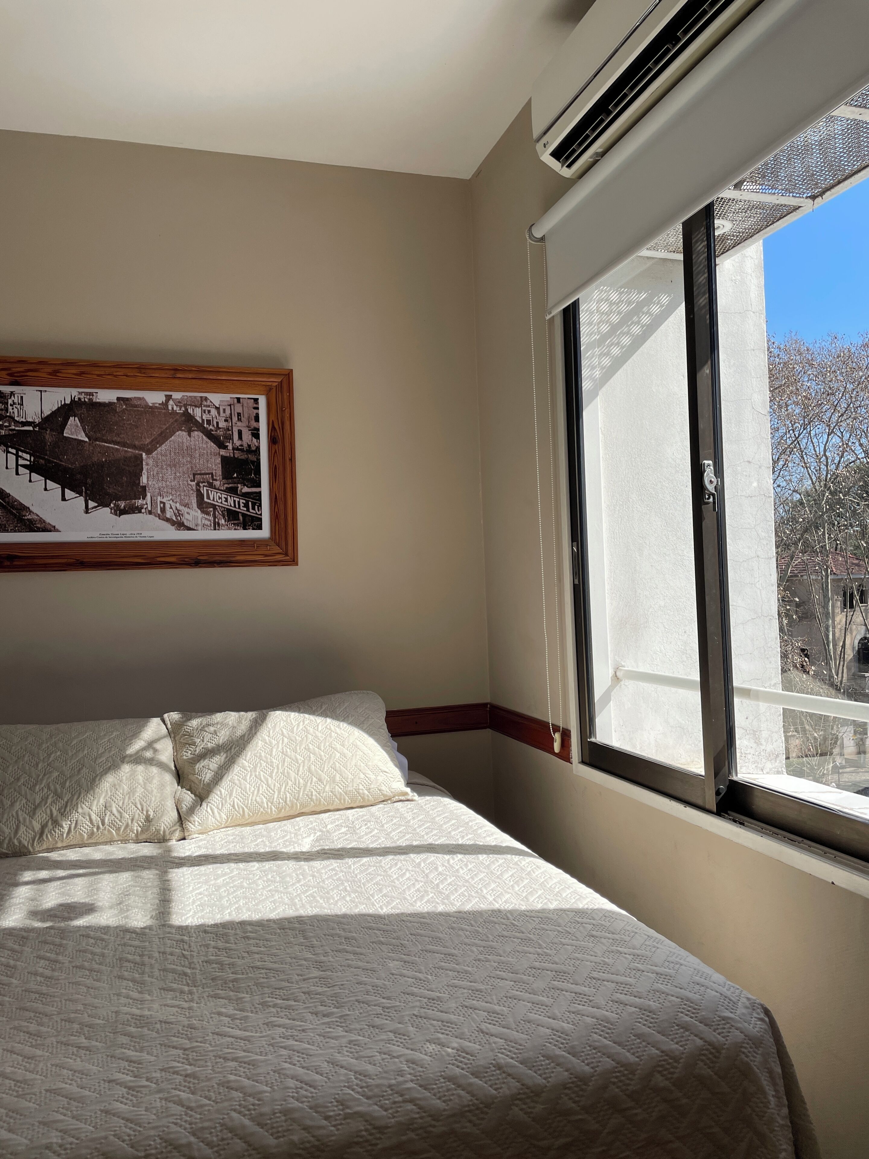 A bedroom with a bed, a window with a view, and a framed picture on the wall.