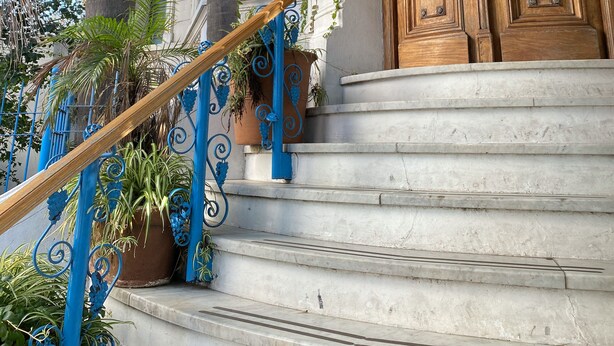 Uma entrada imponente com porta de madeira, toldo azul e escadaria que leva à entrada.