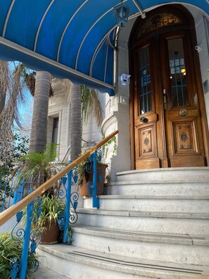 A grand entrance with a wooden door, a blue awning, and a staircase leading to the entrance. - Hotel Vicente Lopez (Vicente Lopez)