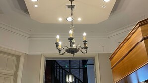 Um saguão de hotel com design de teto moderno, um candelabro e uma escada com corrimão de metal.