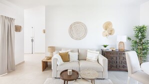 A modern living room with a beige sofa, two round wooden side tables, a dark wooden cabinet, and a white chair. - Lovely apartment for 2 people with WIFI, A/C, TV and terrace (Marbella)