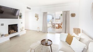A modern living room with a flat-screen TV, a fireplace, a sofa, and a dining area with outdoor seating. - Lovely apartment for 2 people with WIFI, A/C, TV and terrace (Marbella)