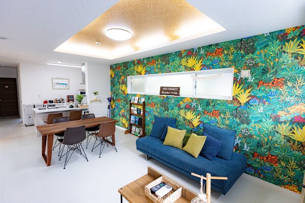 A modern living room with a vibrant floral wallpaper, a blue sofa, and a wooden dining table.
