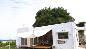 Uma villa moderna e branca com alpendre coberto, área de estar ao ar livre e placa indicando ser uma villa de retiro.