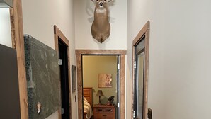 Un pasillo con un venado montado en la pared, suelo de madera y un tapete con estampados de animales.
