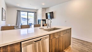 A modern kitchen with a large island, built-in dishwasher, and a flat-screen TV mounted on the wall.