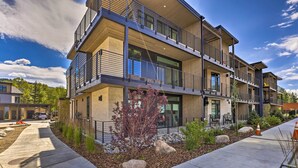 A multi-story residential building with balconies, large windows, and a landscaped front yard.