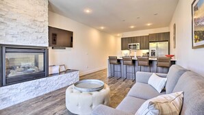 A modern living room with a fireplace, a grey sofa, and a dining area with bar stools.