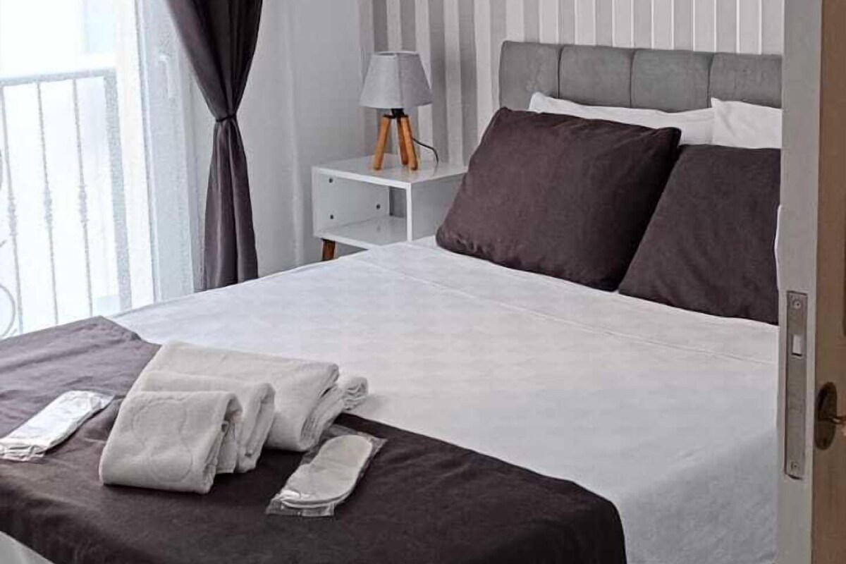 A modern bedroom with a bed, curtains, a nightstand, and a lamp.
