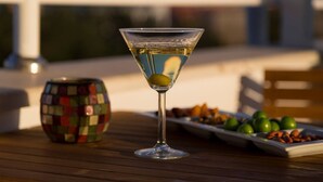 A martini glass with a lemon twist on a wooden table, a mosaic bowl, and a plate of almonds and olives. - Maxxmarine hotel (Izmir)