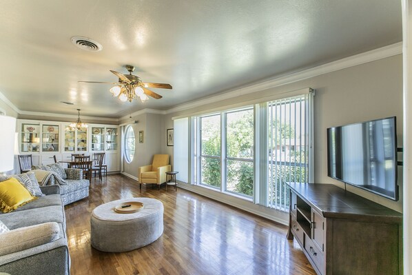 A spacious living room with a large TV, wooden flooring, and a ceiling fan.