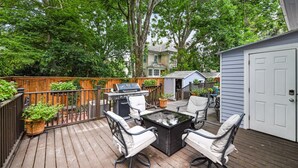 Eine Holzterrasse mit Gartenmöbeln, einem Grill und einem Geräteschuppen.