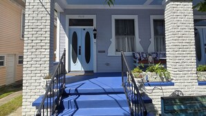 Ein zweistöckiges Haus mit einer blauen Haustür, weißen Backsteinpfeilern und einer kleinen Veranda mit Topfpflanzen.