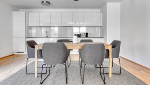 Een moderne keuken met witte kasten, een houten eettafel en vier grijze stoelen.