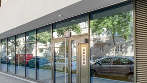Een modern gebouw met een glazen ingang, een zichtbare lift en geparkeerde auto's ervoor.