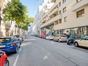 A street lined with parked cars and a building with multiple floors and balconies.