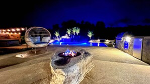 A stone fire pit with a fire, surrounded by a concrete patio. - Charles Town Home w/ Private Pool & Hot Tub (Charles Town)