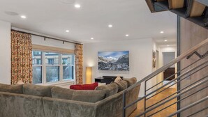 Una sala de estar moderna con un amplio sofá modular, un televisor de pantalla plana y una escalera con barandillas de metal.