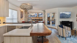 Una cocina moderna con una isla central, un comedor con sillas a rayas y un amplio ventanal con vistas a la montaña.