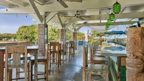Un espace de restauration en plein air avec des chaises et des tables en bois, des ventilateurs de plafond et des lanternes suspendues.