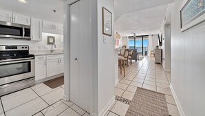 A modern kitchen with white cabinets, stainless steel appliances, and a dining area with a view. - Summerchase 304- Family Friendly Fun Beach Getaway!! (Orange Beach)
