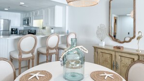 A dining area with a round table, chairs, a decorative glass bottle, and a woven pendant light. - Summerchase 304- Family Friendly Fun Beach Getaway!! (Orange Beach)