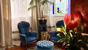 Une pièce avec un lustre, deux fauteuils bleus, un pouf rond, une plante en pot et un plancher en bois.