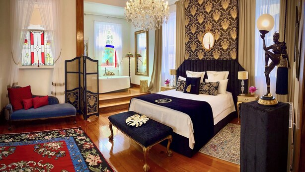Une chambre à coucher luxueuse, dotée d’un grand lit, d’un lustre, d’une statue et offrant une vue sur une pièce avec une fenêtre et un miroir.