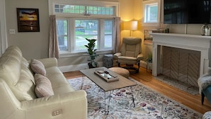 Una sala de estar con sofá, sillón, mesa de centro, chimenea, televisor y vistas al exterior.