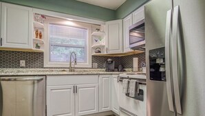 Eine Küche mit weißen Schränken, einem Edelstahl-Kühlschrank, einem Fenster mit Jalousien und einer Spritzschutzwand mit sechseckigen Fliesen.