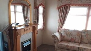 A living room with a fireplace, a television, and a floral sofa. - Remarkable 2-Bed Caravan  in Ingoldmells (Ingoldmells)