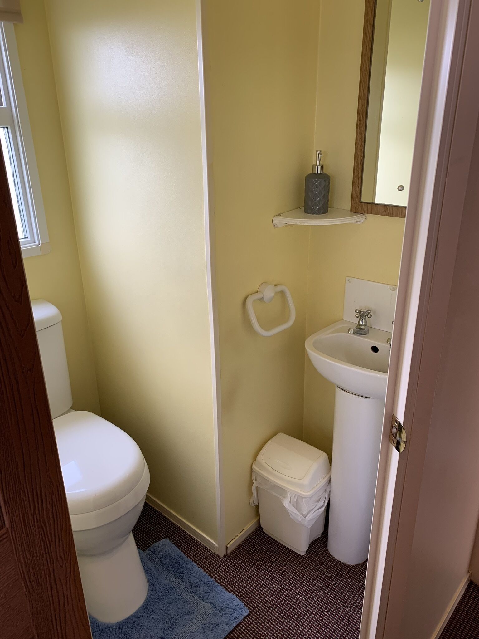 A small bathroom with a toilet, sink, and a small storage bin.