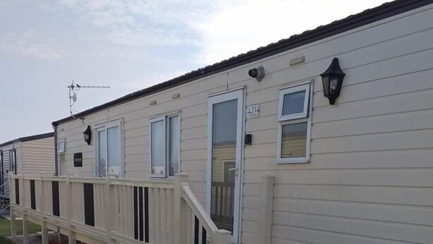 A row of mobile homes with a wooden deck and a small staircase leading to the entrance. - Remarkable 2-Bed Caravan  in Ingoldmells (Ingoldmells)
