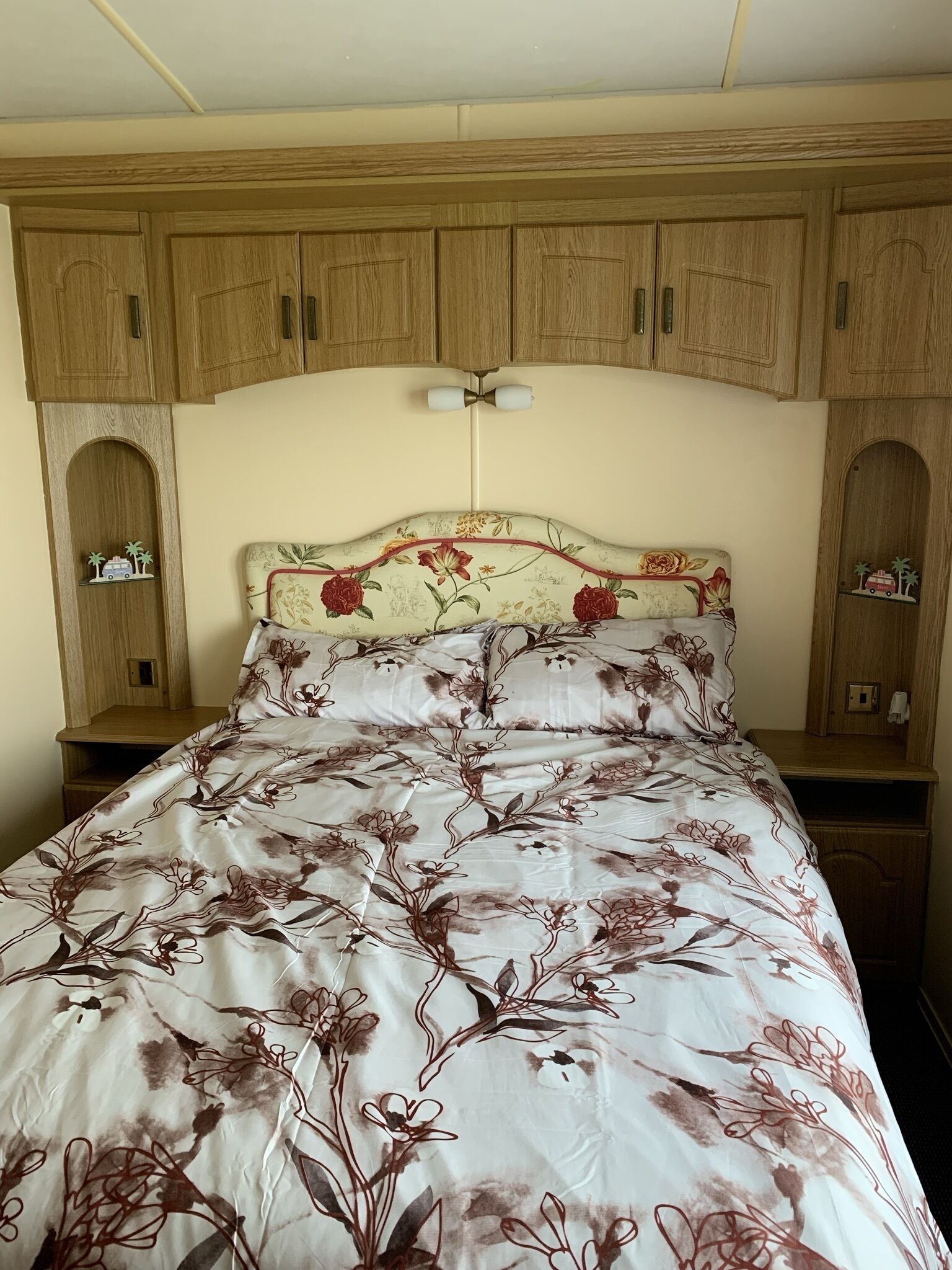 A bedroom with a floral bedspread, wooden cabinets, and a nightstand.