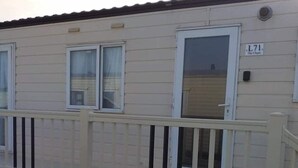 A single-story mobile home with a beige exterior, a white door, and a small porch with a white railing. - Remarkable 2-Bed Caravan  in Ingoldmells (Ingoldmells)
