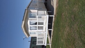 A white mobile home with multiple windows and a balcony, situated on a grassy area with a clear sky.