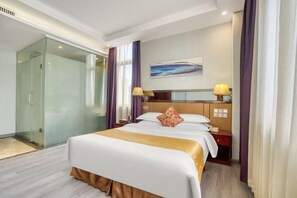 A hotel room with a large bed, a glass-enclosed shower, a desk with a lamp, and a painting on the wall.