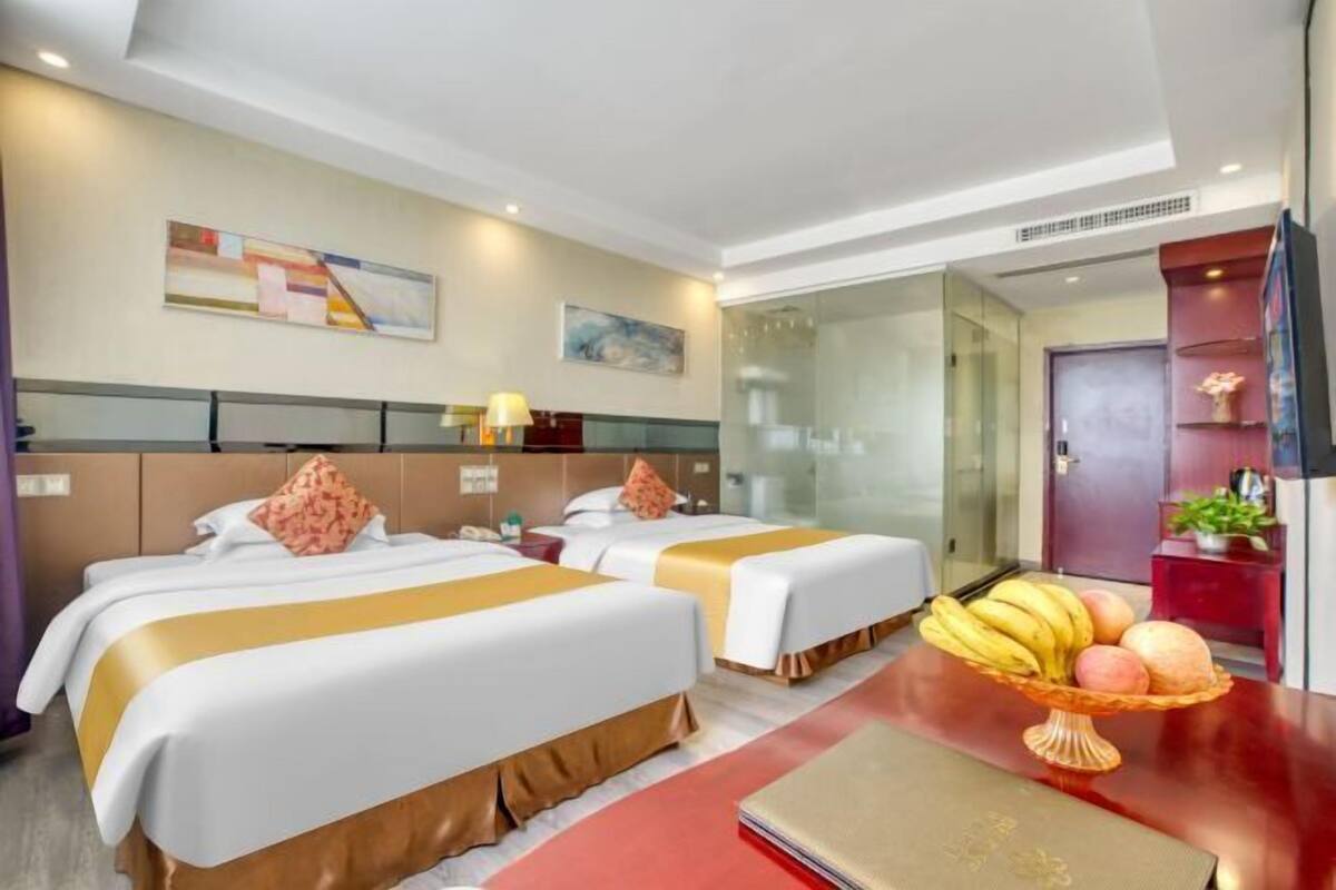 Una habitación de hotel con dos camas, una mesa roja y una cesta de frutas.
