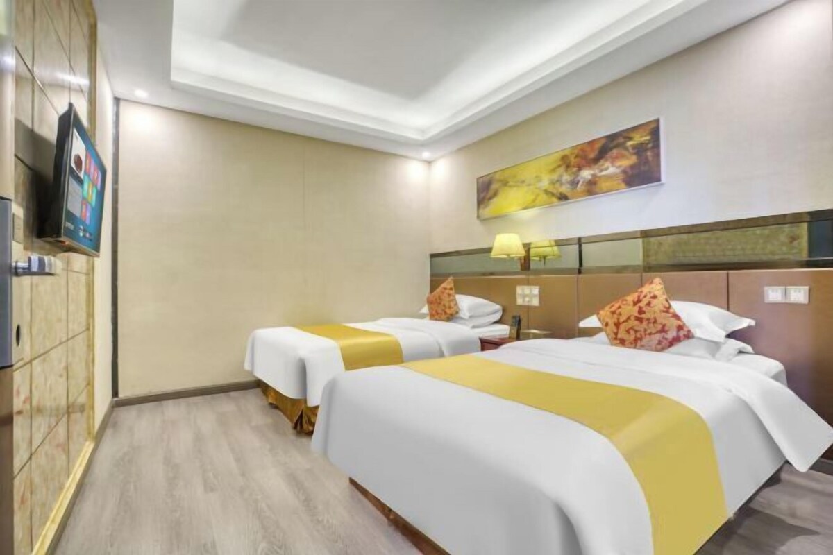 A hotel room with two beds, a TV, a painting, and a lamp.