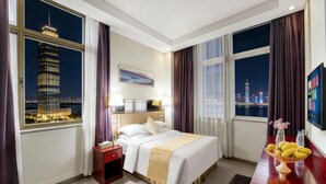 Une chambre d’hôtel avec un lit, une table de chevet et un bureau sur lequel se trouve un panier de fruits.
