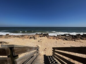 A wooden bench leading to a rocky beach with waves crashing onto the shore.