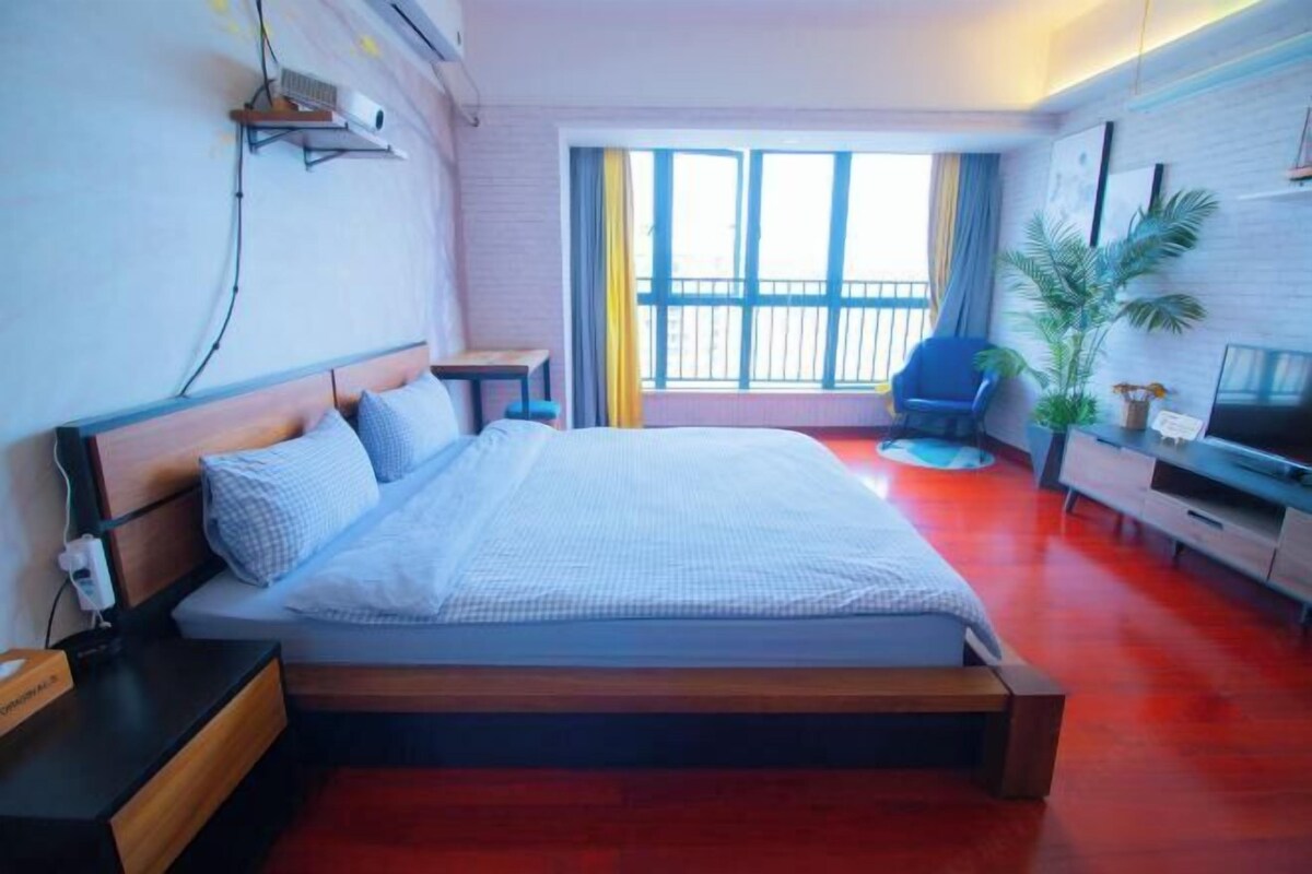 A hotel room with a bed, a desk, a chair, a TV, and a balcony with curtains.