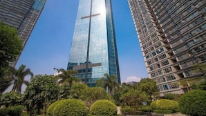 A tall, modern skyscraper with a glass facade, surrounded by lush greenery and other high-rise buildings. - Huizhou Kaisa Musi Hotel Apartment (Huizhou)
