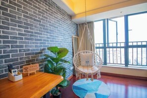 Una habitación con pared de ladrillo, una silla colgante, una mesa redonda con una planta y una ventana con vistas.