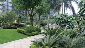 A landscaped garden with various plants and trees, a paved walkway, and a building in the background. - Huizhou Kaisa Musi Hotel Apartment (Huizhou)