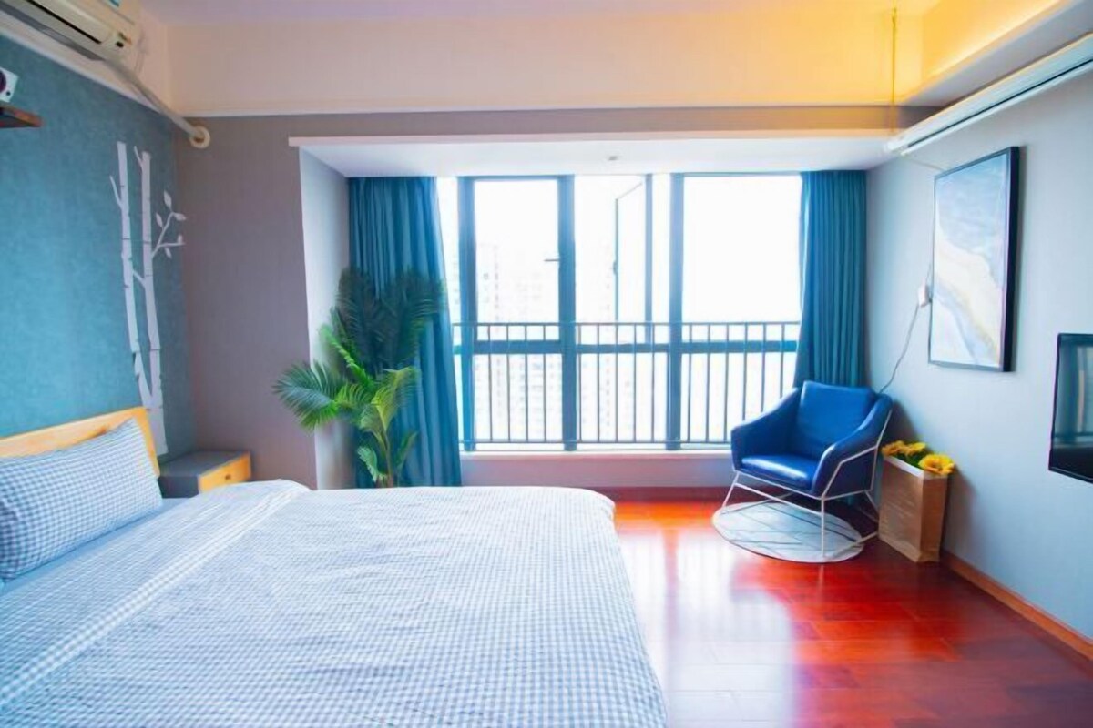 A hotel room with a bed, a chair, a large window, and a plant.