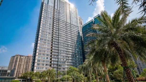 A high-rise building with a modern glass facade, surrounded by palm trees and a small water feature. - Huizhou Kaisa Musi Hotel Apartment (Huizhou)