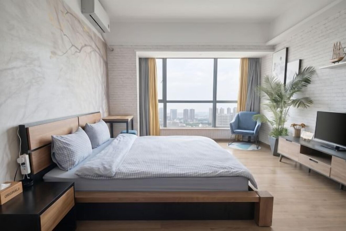 A modern bedroom with a large bed, a TV, and a city view.